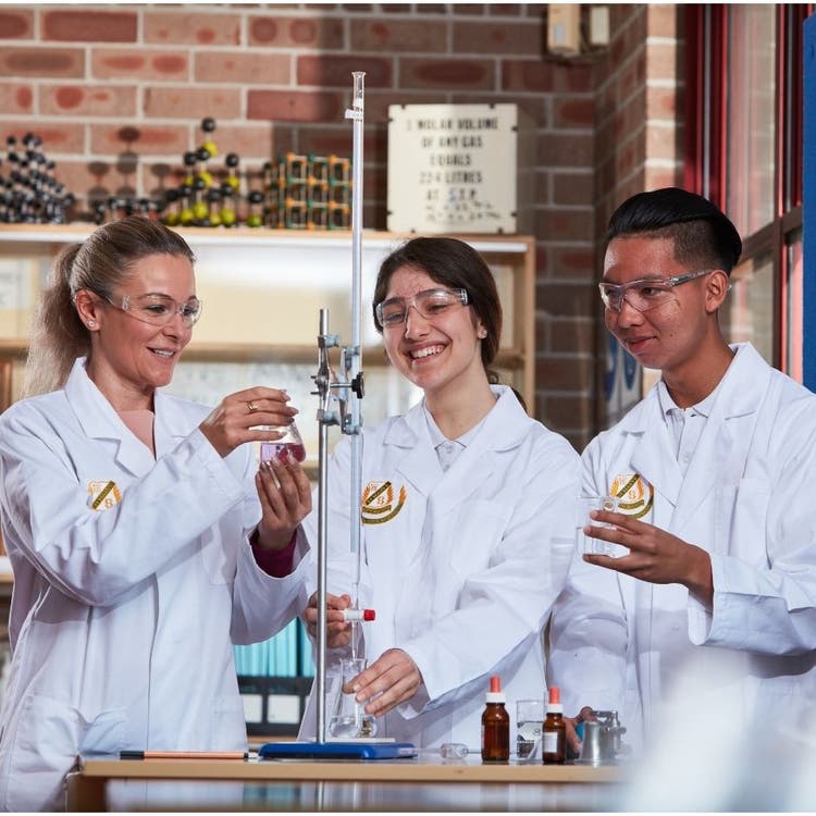 A science teacher working with two students on an experiment in a science lab, using different equipment and containers of chemicals.