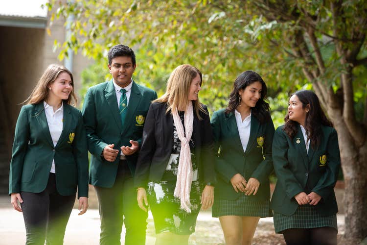 Four students in green blazers and school dress code, walking with the principal in the school grounds.