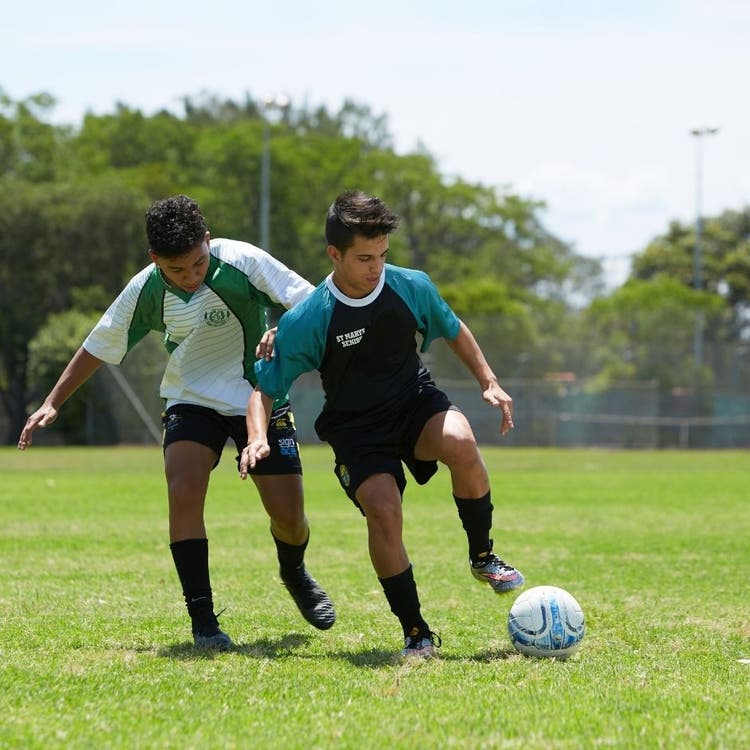Two young men on a soccer field, both trying to kick the soccer ball