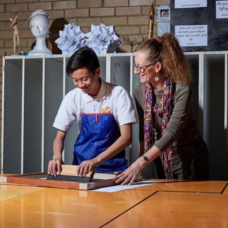 A student and a teacher, working on creating a printed work in an art classroom
